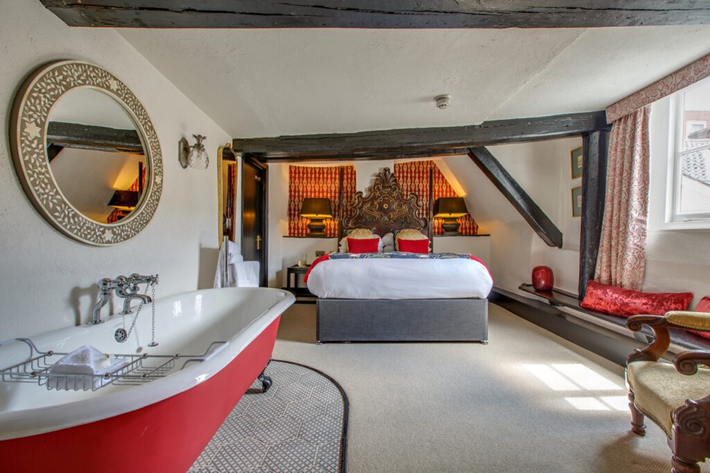 A red roll-top bath at the foot of the bed