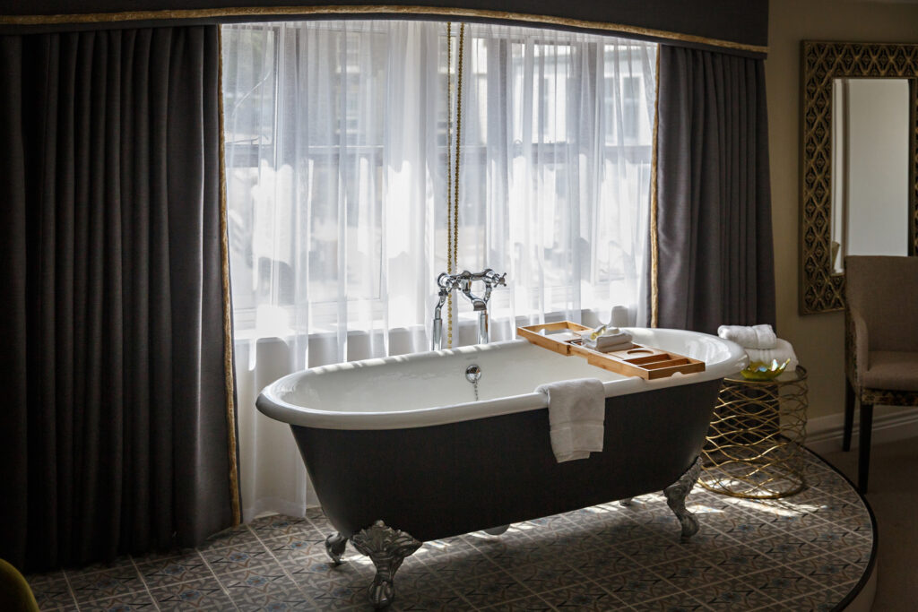 A dark roll-top bath by tall curtained windows